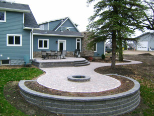 Blue House with Raised Patio and Fire Pit by Oasis Landscapes