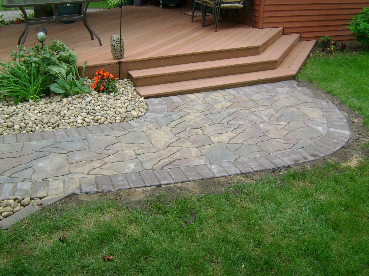 deck stepping down to paver walkway and softscapes by Oasis Landscapes