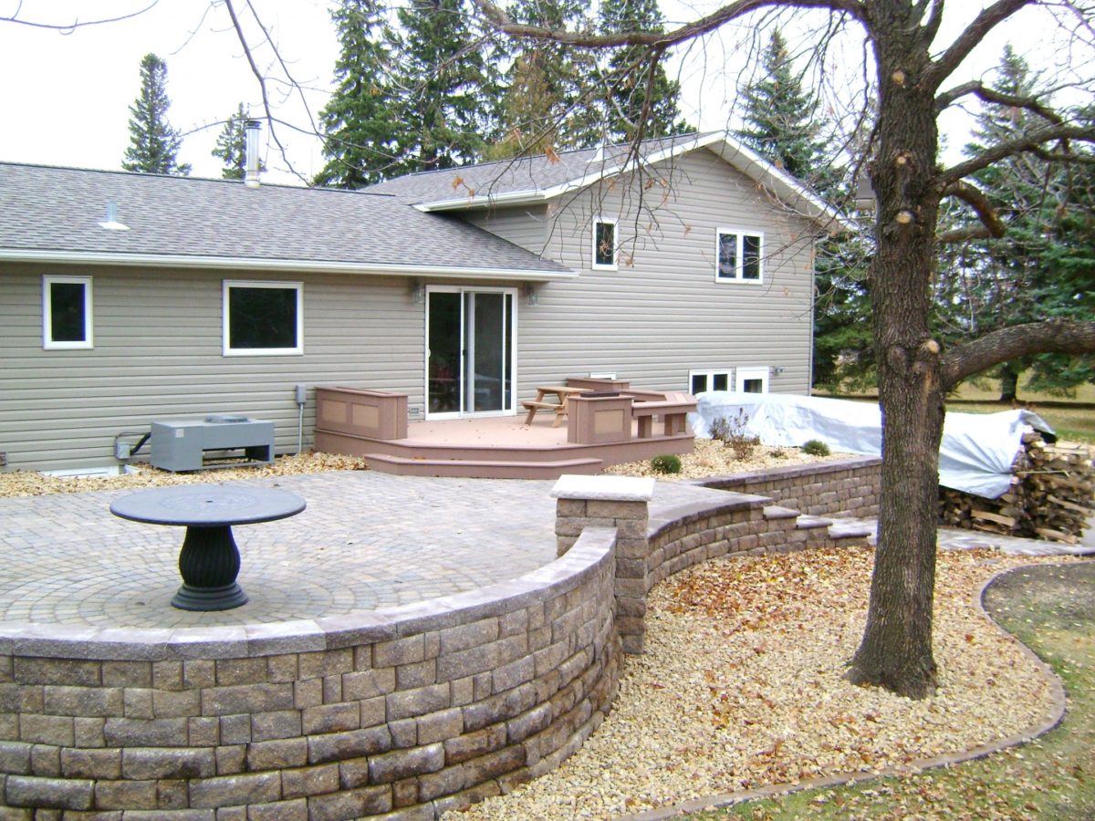 raised paver patio with retaining walls, stairs, deck, and seating wall