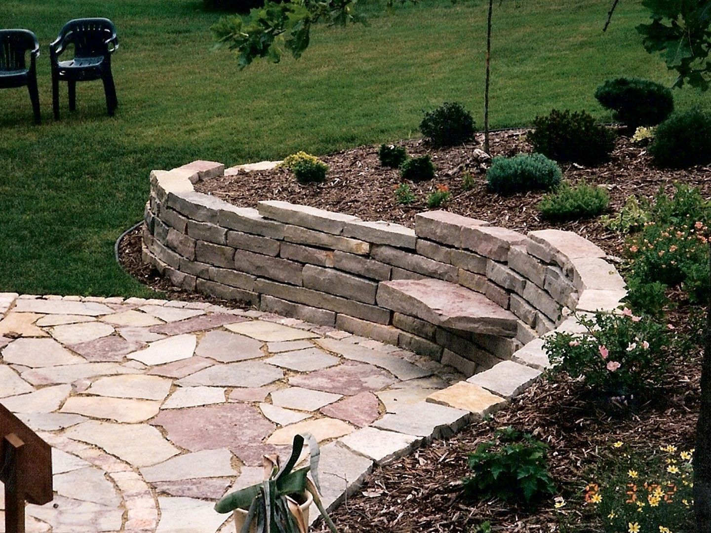 Large stone retaining wall with sitting stones by Oasis Landscapes